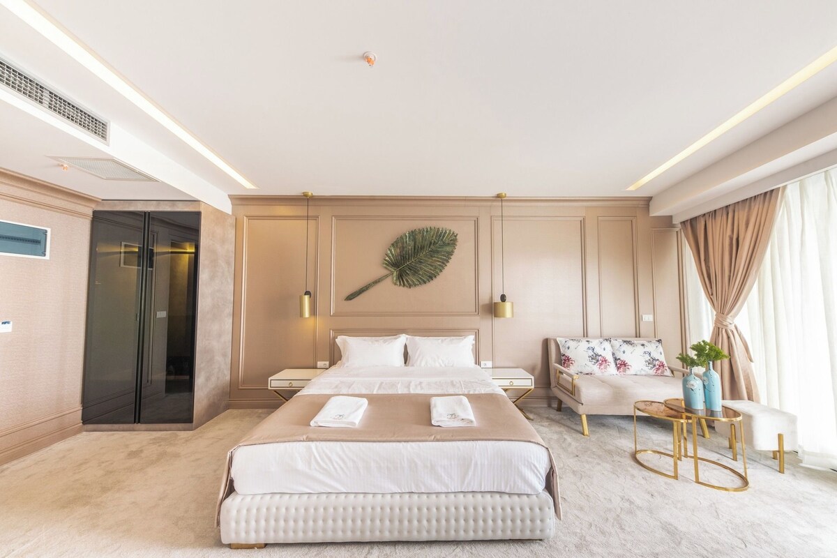 A hotel room with a large bed, a sofa, a small table, and a decorative leaf on the wall.