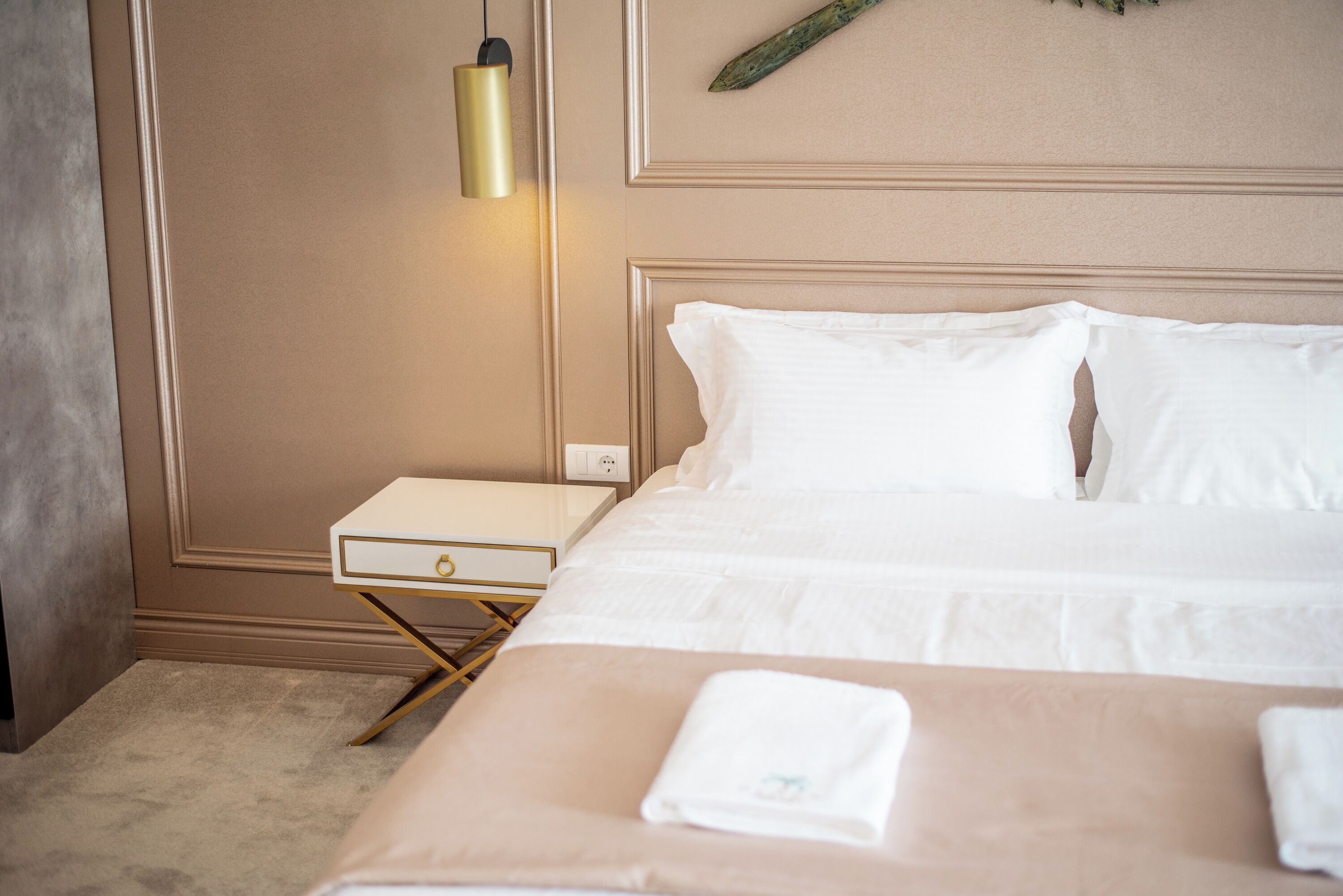 A hotel room with a bed, bedside table, lamp, and a wall-mounted decorative element.