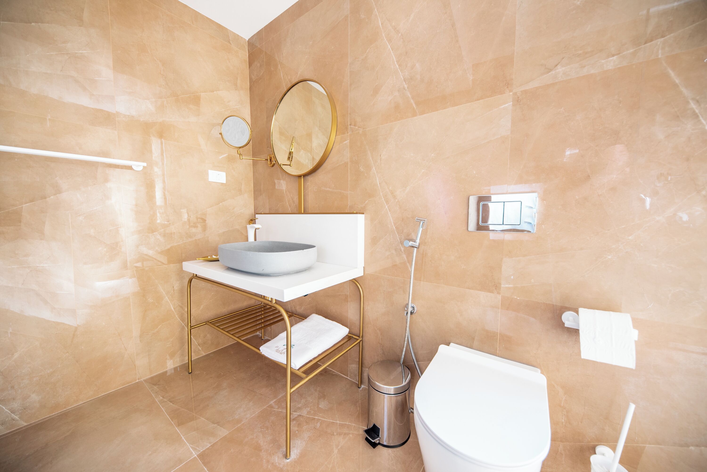 A modern bathroom with a white sink, gold fixtures, a round mirror, and a toilet.