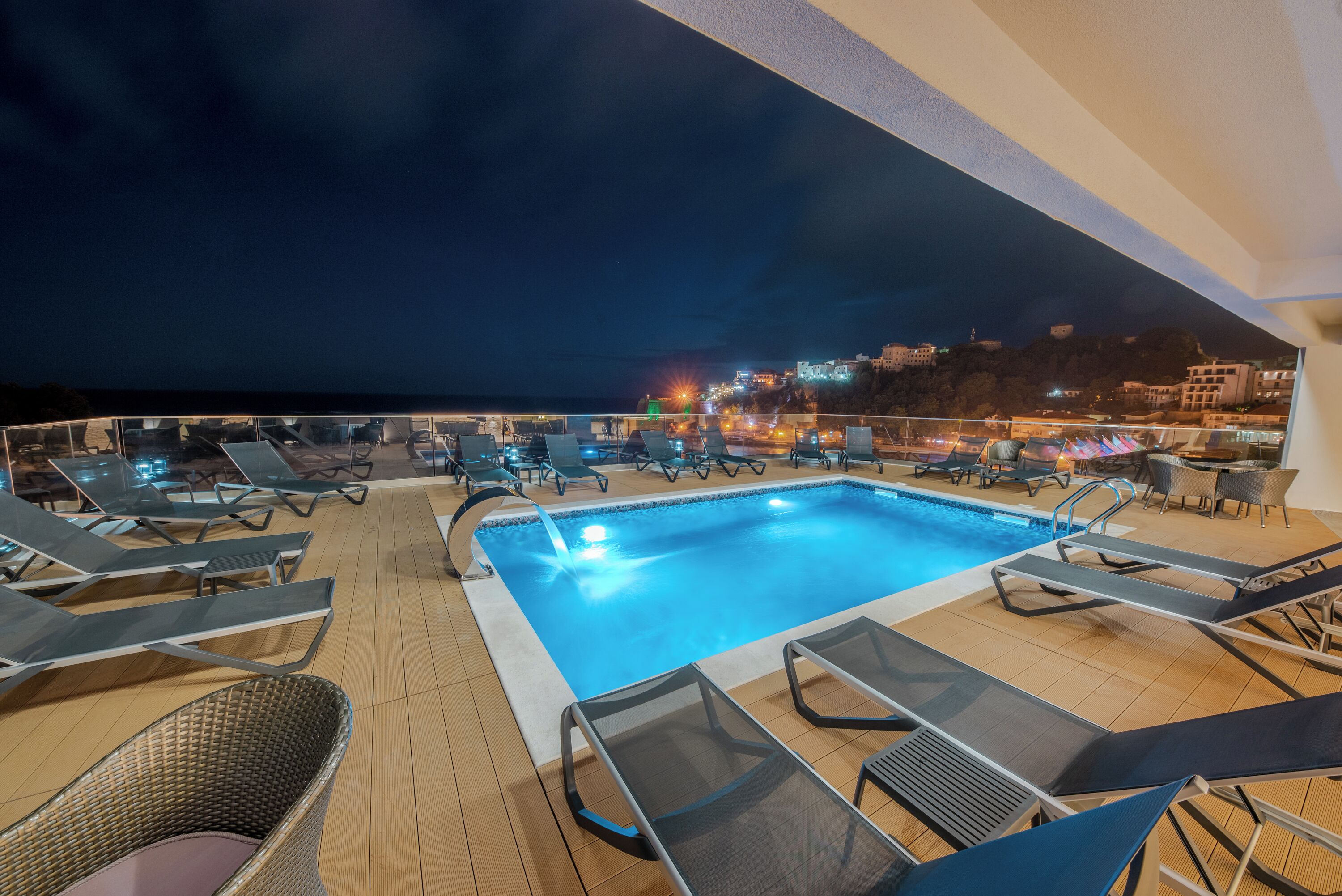 A pool area with lounge chairs and a view of the city at night.