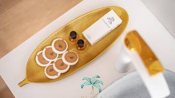 Un plateau orné d’un motif en forme de feuille, contenant plusieurs objets ronds, une boîte blanche avec du texte et une bouteille blanche avec un bouchon doré.
