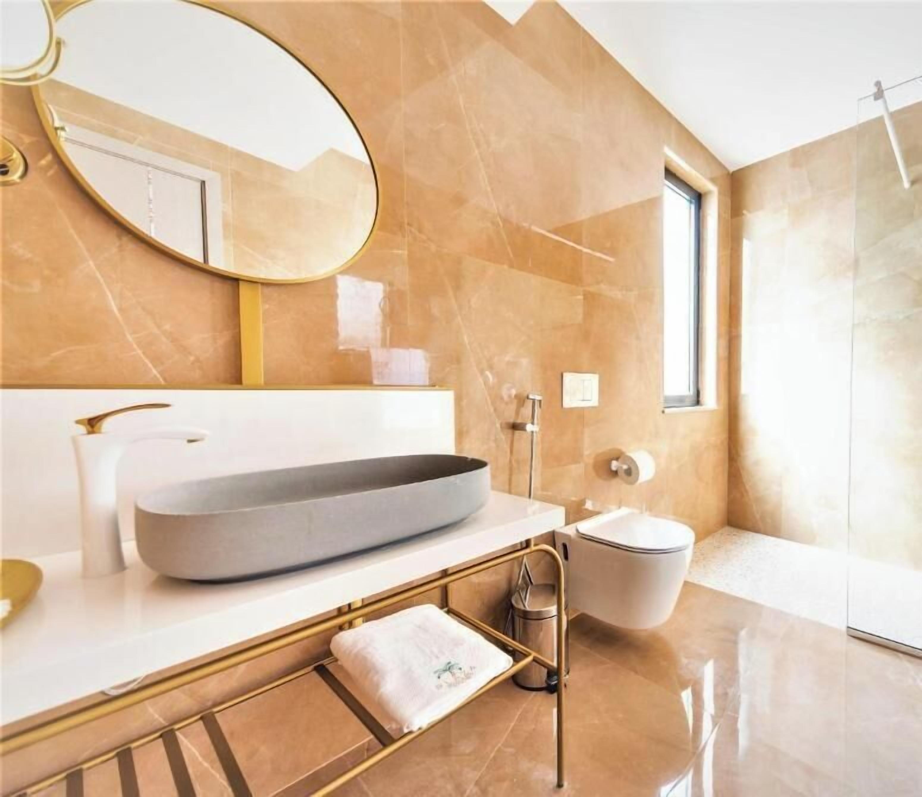 A modern bathroom with a large oval mirror, a freestanding bathtub, and a glass-enclosed shower area.