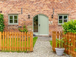 A brick house with a green door, two windows, a wooden fence, and a potted plant. - 3 Bed in Church Stretton (oc-76621) (Rushbury)