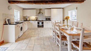 A kitchen with white cabinets, a wooden beam ceiling, a dining table with chairs, and a washing machine. - 3 Bed in Church Stretton (oc-76621) (Rushbury)
