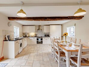 A kitchen with white cabinets, a wooden beam ceiling, a dining table with chairs, and a washing machine. - 3 Bed in Church Stretton (oc-76621) (Rushbury)