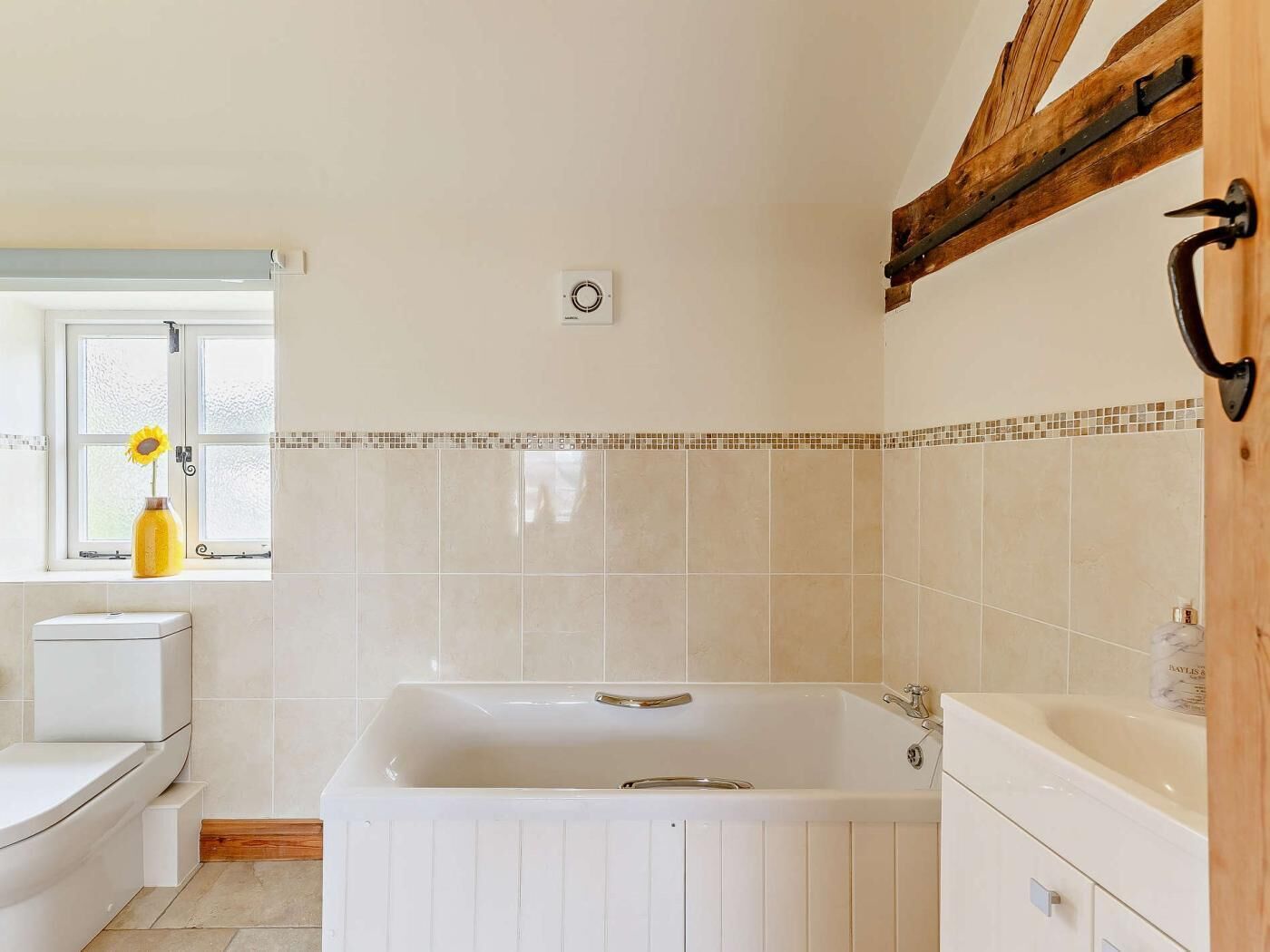 A bathroom with a bathtub, toilet, and window with a sunflower.