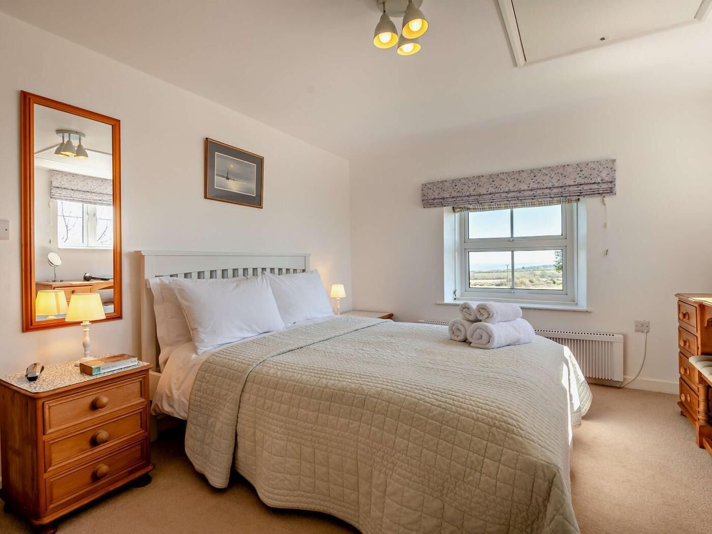 A bedroom with a bed, a dresser, a mirror, a window with a view, and a ceiling light fixture.