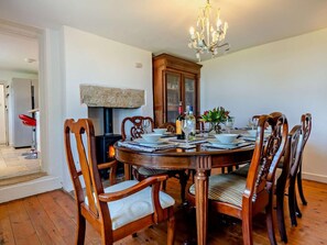 Ein Esszimmer mit rundem Tisch, Holzstühlen, einer Chandelüster und einem Kaminofen.