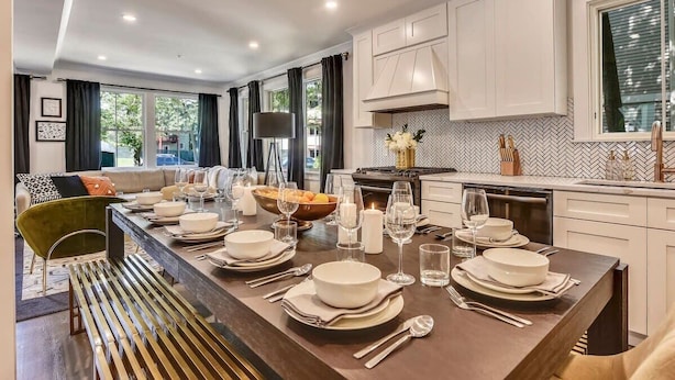 Una cocina moderna con armarios blancos, una isla central con comedor y vista al exterior.