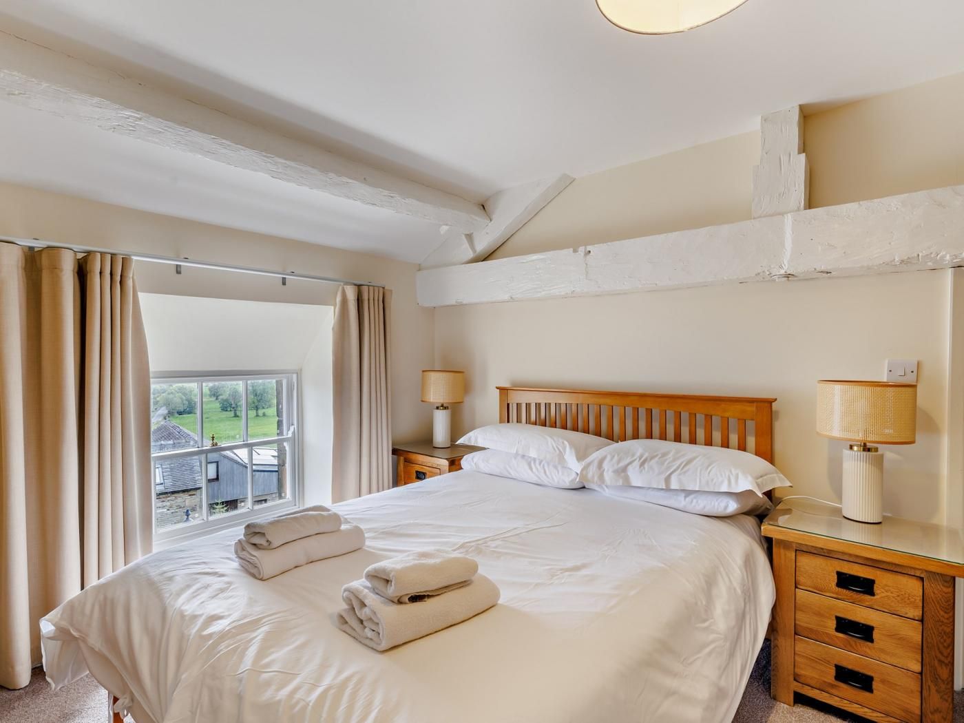 Una habitación de hotel con una cama grande, dos mesitas de noche, una ventana con cortinas y vistas al exterior.