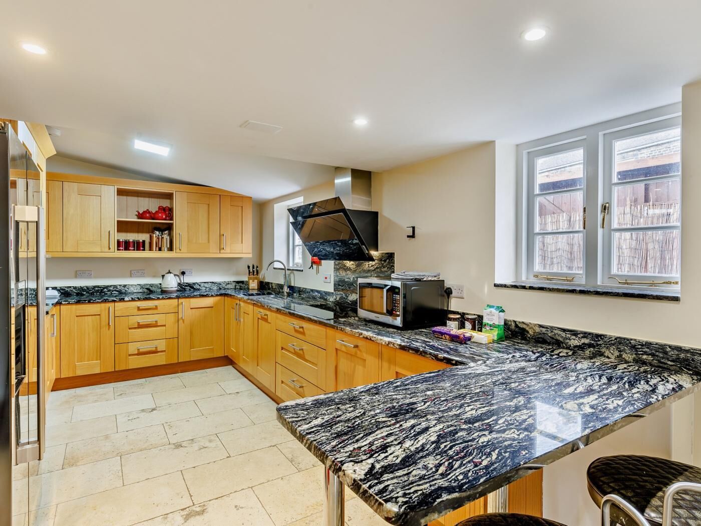 A kitchen with wooden cabinets, a granite countertop, a microwave, and a window with blinds.