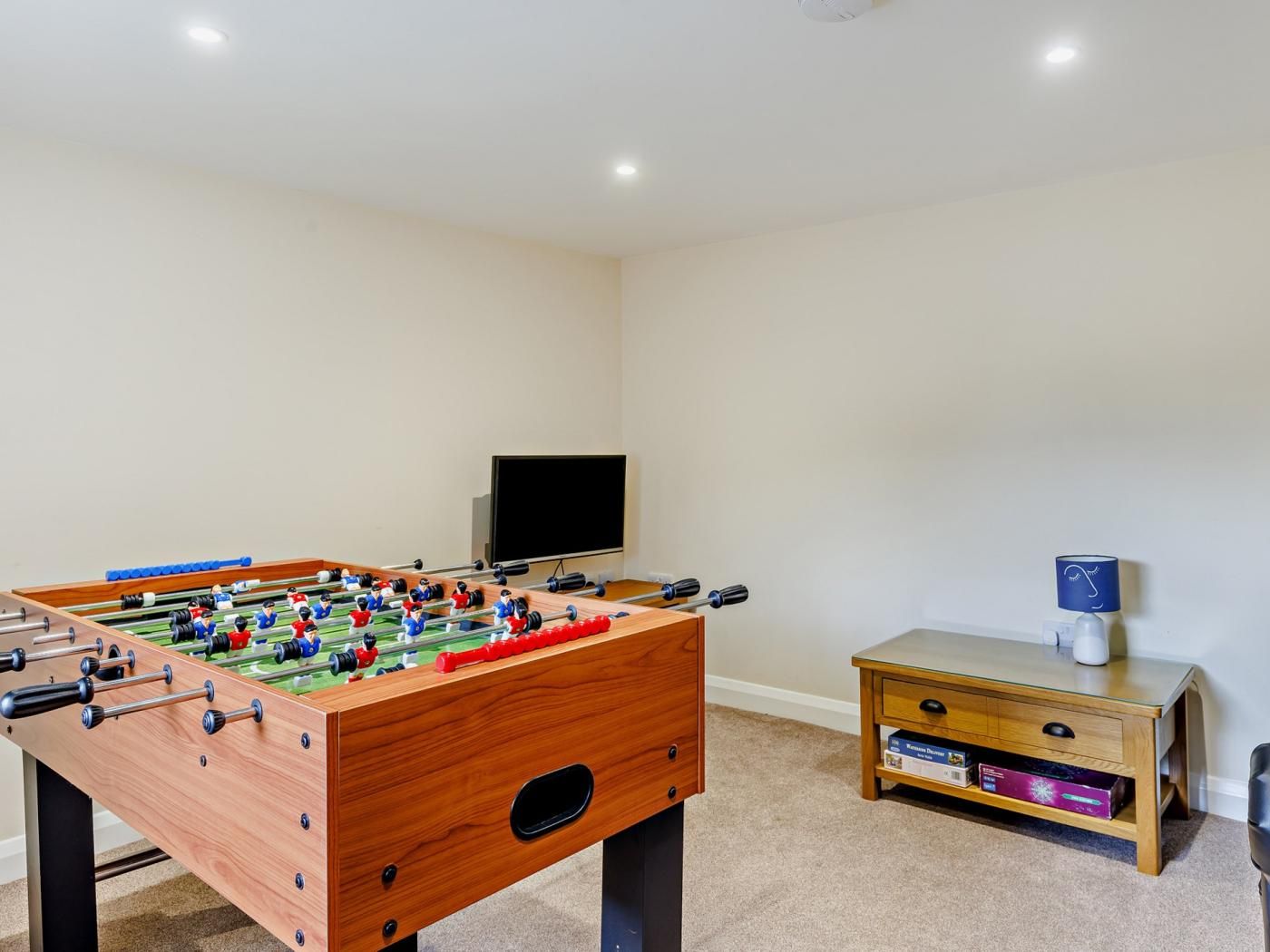 Een kamer met een tafelvoetbaltafel, een televisie en een klein houten dressoir.