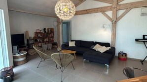Ein großzügiger Wohnraum mit hohen Decken, einem dunklen Sofa, zwei Korbstühlen, einem Holztisch und einem einzigartigen runden Kronleuchter.