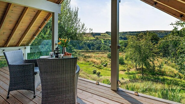 Een overdekt terras met rieten meubels, een tafel met koffiepot en uitzicht op een groen landschap.