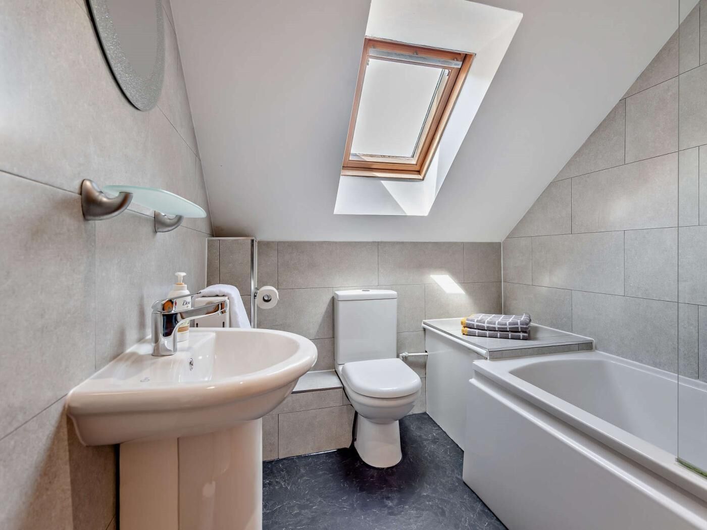 A modern bathroom with a skylight, a sink, toilet, and bathtub.