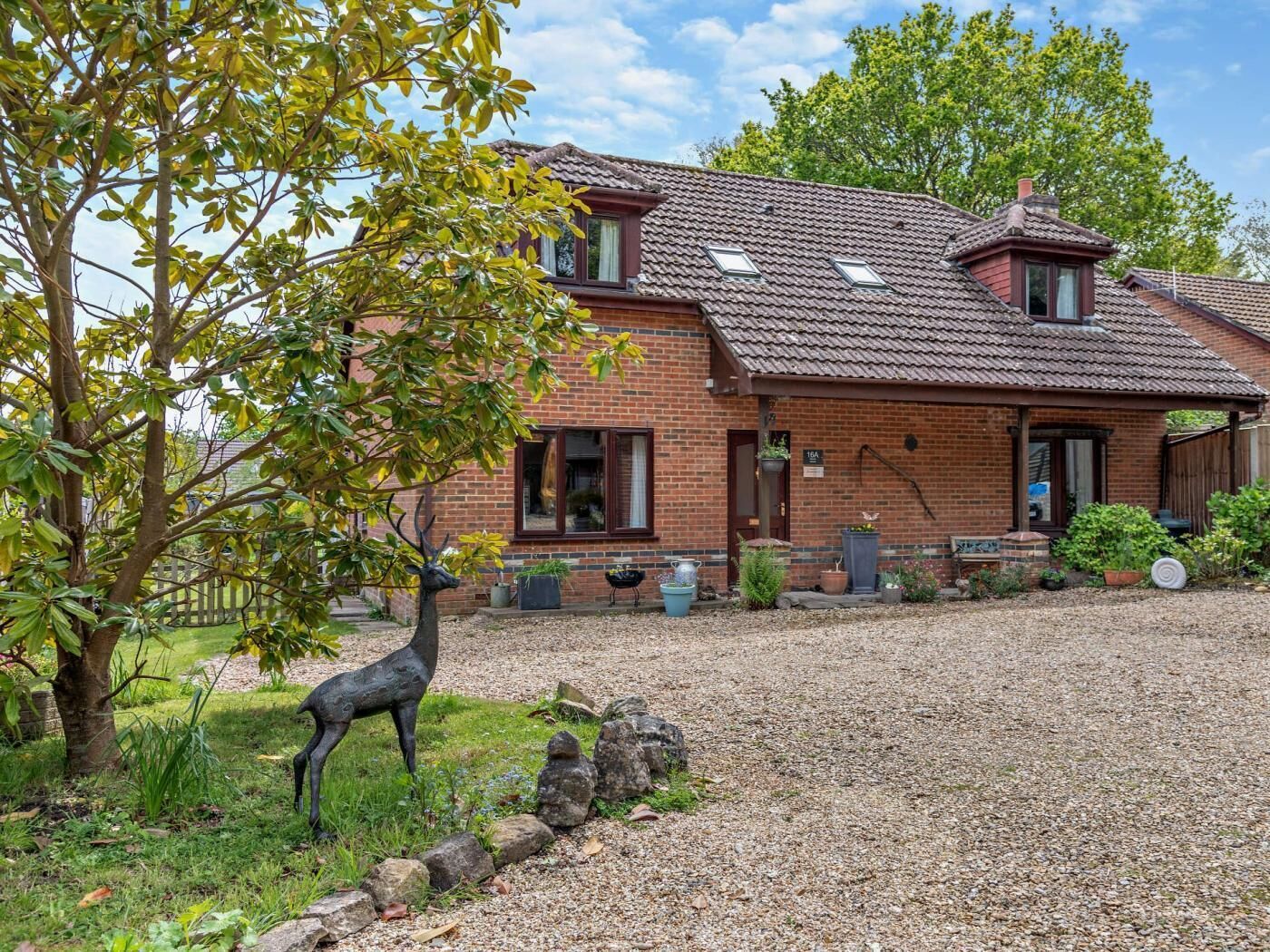 A two-story brick house with a gravel driveway, a front porch, and a statue of a deer.