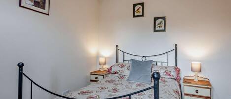 A bedroom with a metal bed frame, floral bedding, two bedside tables with lamps, and framed pictures on the wall.
