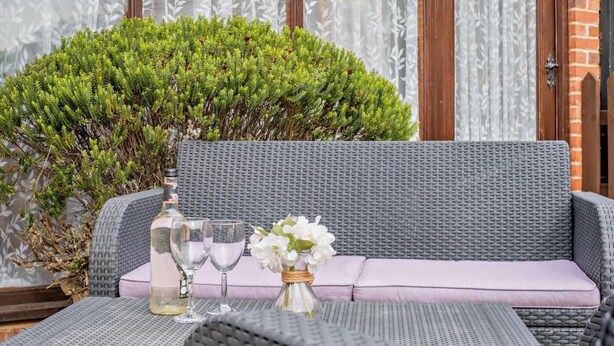 A wicker sofa with a cushion, a small table with a bottle and glasses, and a potted plant. - 2 Bed in King's Lynn (oc-77764) (Tattersett)