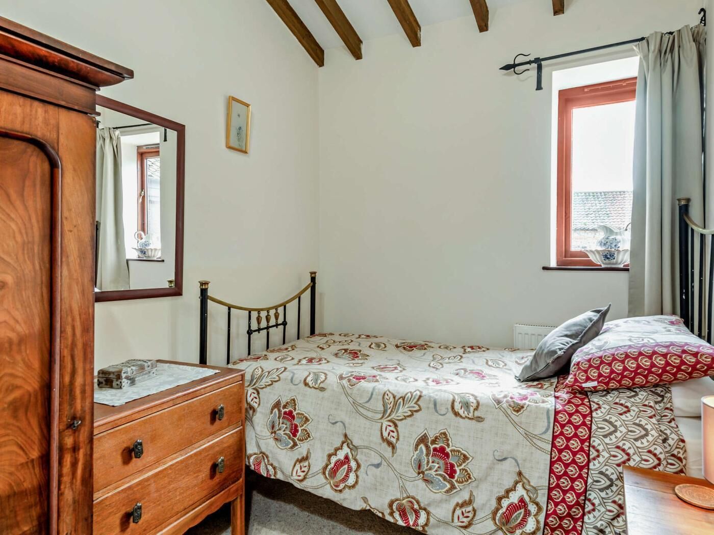 Une chambre à coucher comprenant un lit, une commode, un miroir, une fenêtre et donnant sur l’extérieur.
