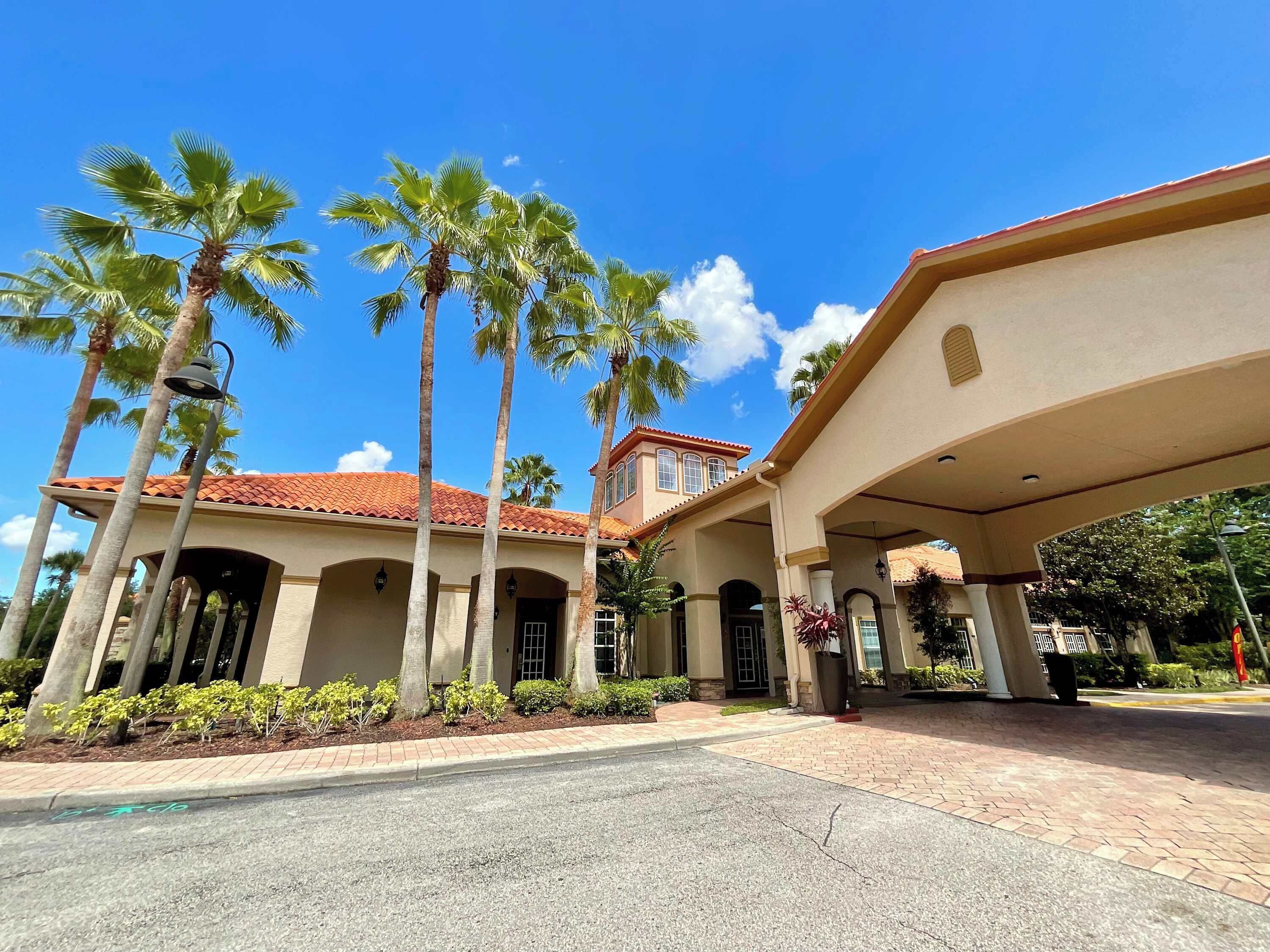 A building with a red-tiled roof, palm trees, and a covered entrance area.