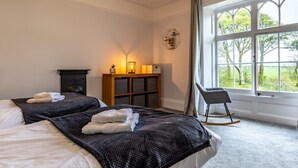 Un dormitorio con dos camas, un armario de madera, una mecedora y un amplio ventanal con vistas a árboles.