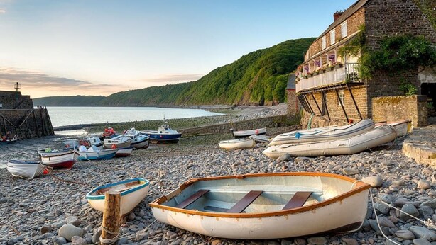 Una playa de guijarros con barcos, un edificio de piedra con balcón y vistas al mar.