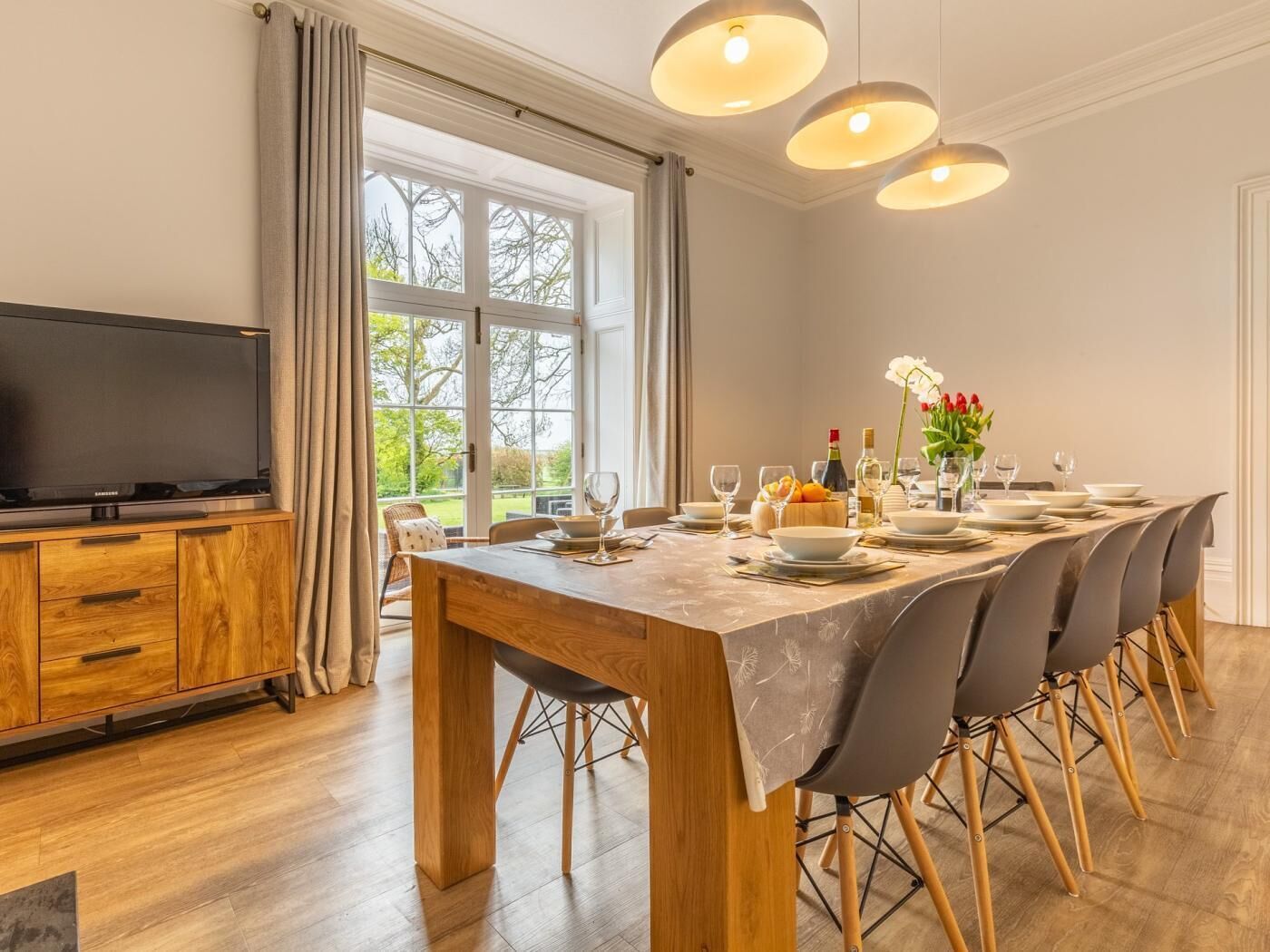 Un espace repas comprenant une table en bois, des chaises, un téléviseur et une vue sur l’extérieur.