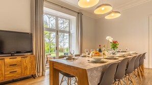 Un comedor con mesa de madera, sillas, televisor y vistas al exterior.