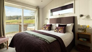 A bedroom with a large bed, a window with a view of a lake, a bedside table with a lamp, and a small bedside table with a book. - 2 Bed in Castle Douglas (oc-77837) (Auchencairn)