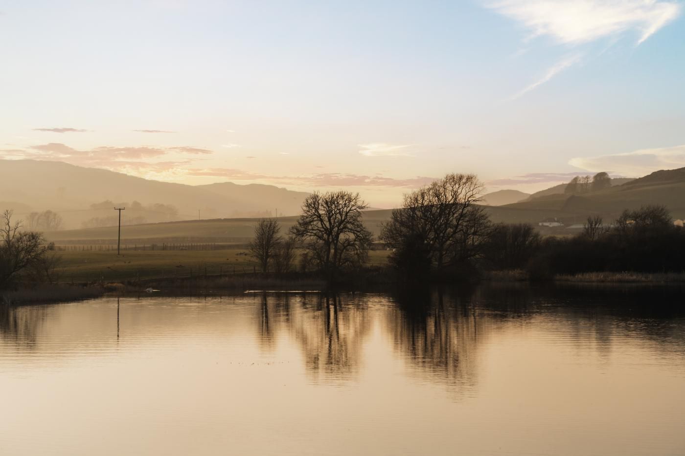 Aigua tranquil·la que reflecteix arbres i turons allunyats.