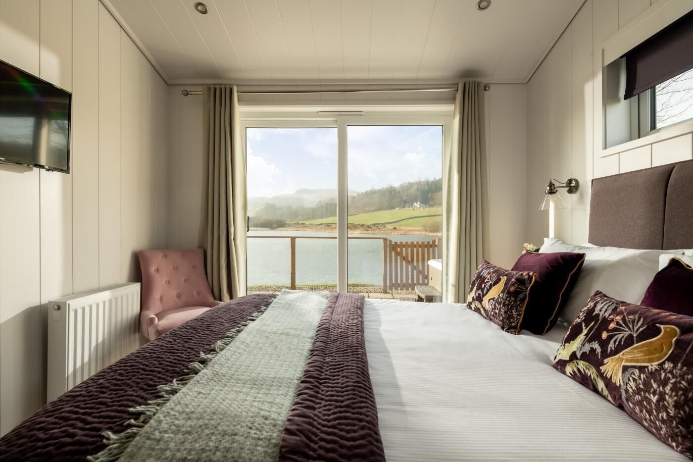 A bedroom with a large bed, a chair, a view of a lake, and a balcony.