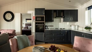 A modern kitchen with dark cabinets, a microwave, oven, and a dining area with a table set for two. - 2 Bed in Castle Douglas (oc-77837) (Auchencairn)