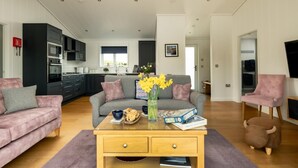 A modern living room with a sofa, coffee table, and a kitchen in the background. - 2 Bed in Castle Douglas (oc-77837) (Auchencairn)