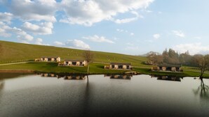 A tranquil lakeside setting with a row of buildings, a grassy hill, and a clear sky. - 2 Bed in Castle Douglas (oc-77837) (Auchencairn)