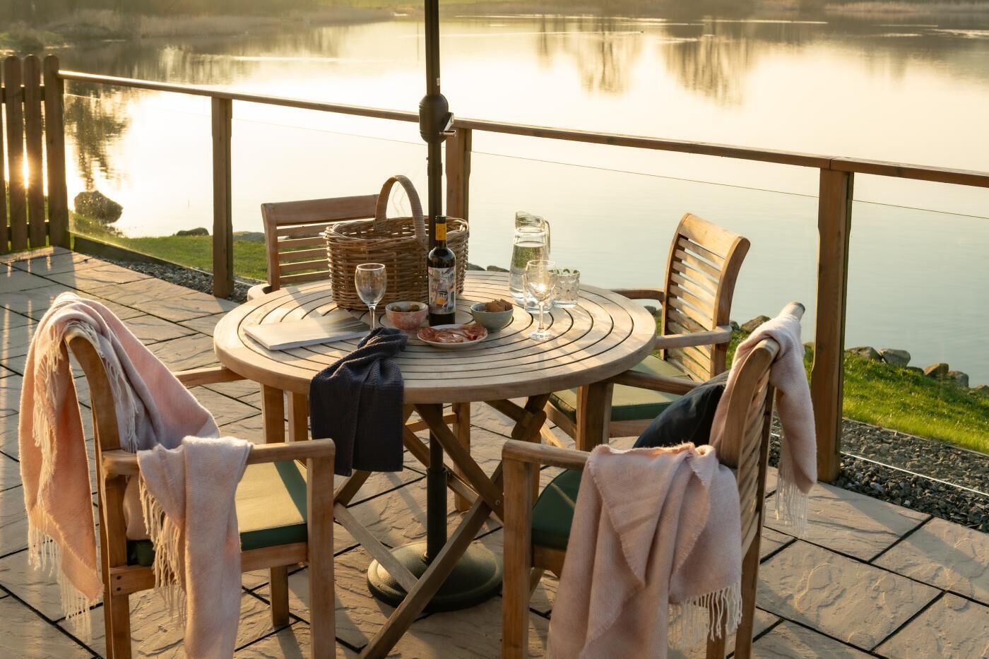 A round wooden table with chairs, a basket, a bottle, glasses, and a plate of food.