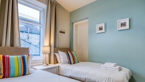 A hotel room with two beds, a window with curtains, a lamp, and two framed pictures on the wall. - 3 Bed in Buxton (oc-77955) (Tideswell)