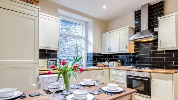 A modern kitchen with white cabinets, a black tiled backsplash, and a wooden dining table set for four. - 3 Bed in Buxton (oc-77955) (Tideswell)