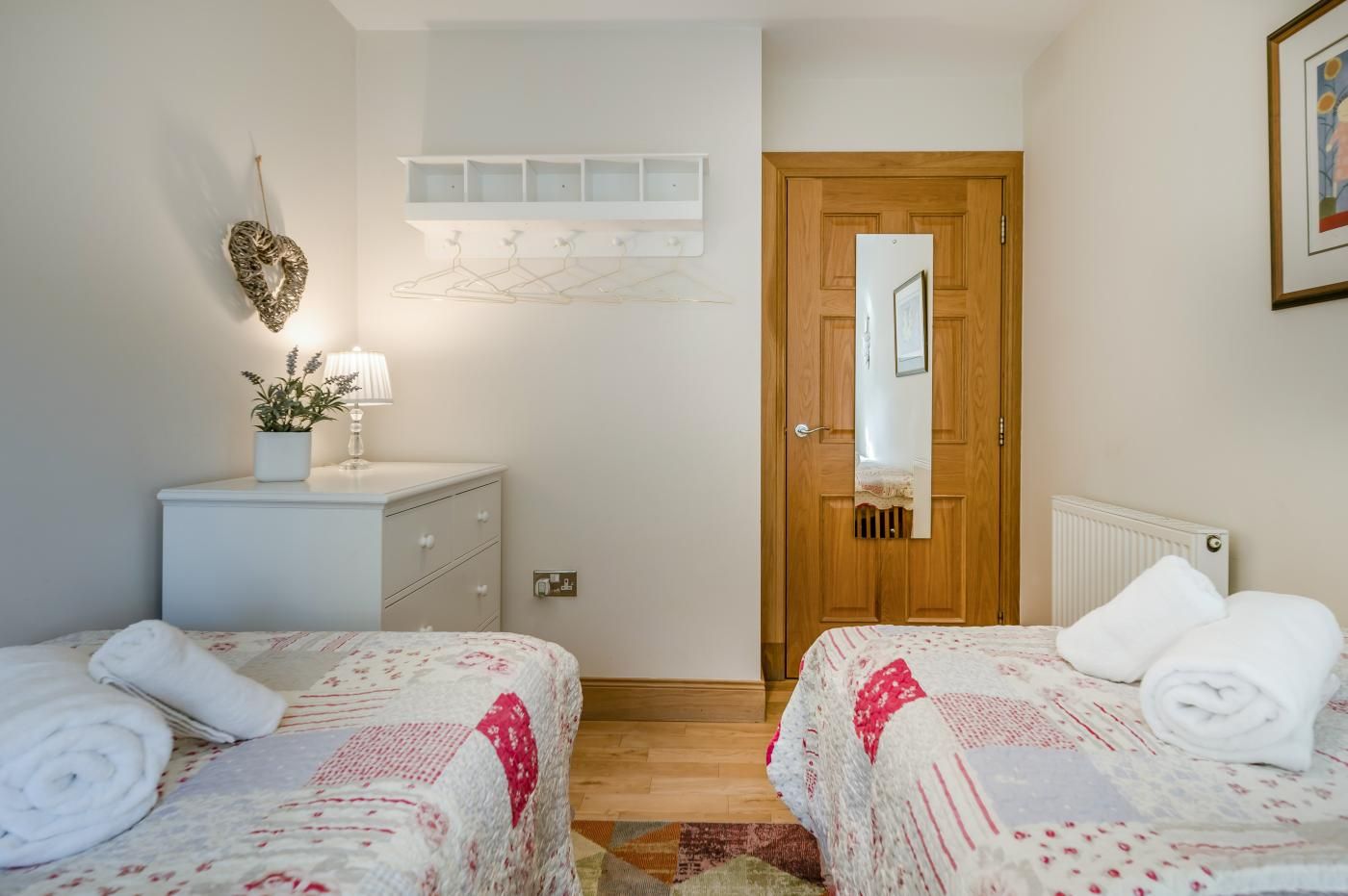 A bedroom with two beds, a dresser, a mirror, a radiator, and a door.
