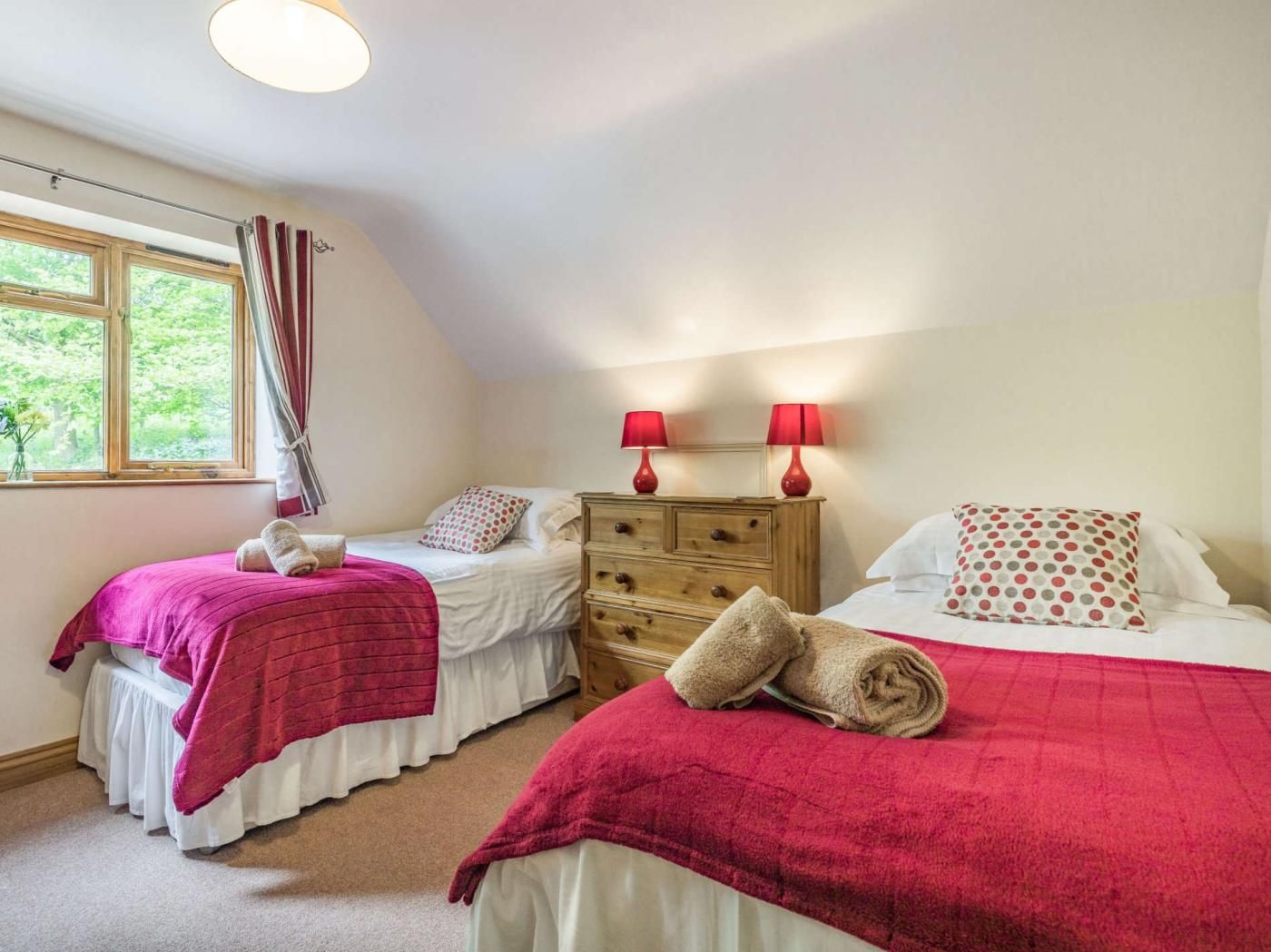 A bedroom with two beds, a dresser, and a window with curtains.