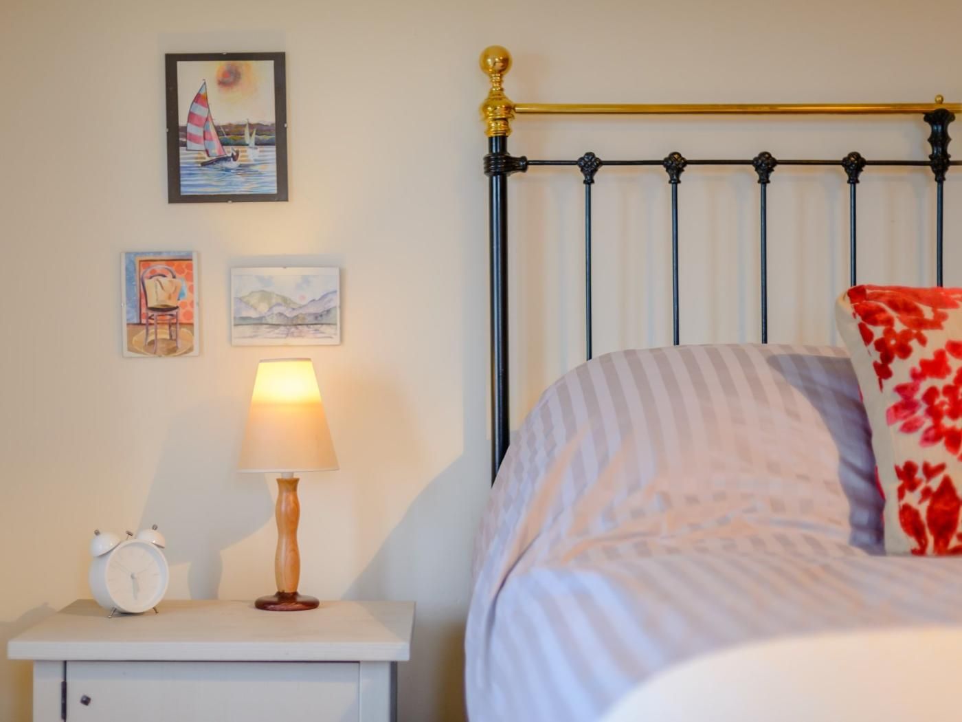 Un dormitorio con cama, una mesita de noche con lámpara y dos cuadros enmarcados en la pared.