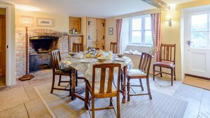 A dining room with a brick fireplace, wooden chairs, a table set for four, and a window with curtains. - 4 Bed in Wareham (oc-78042) (Kingston)