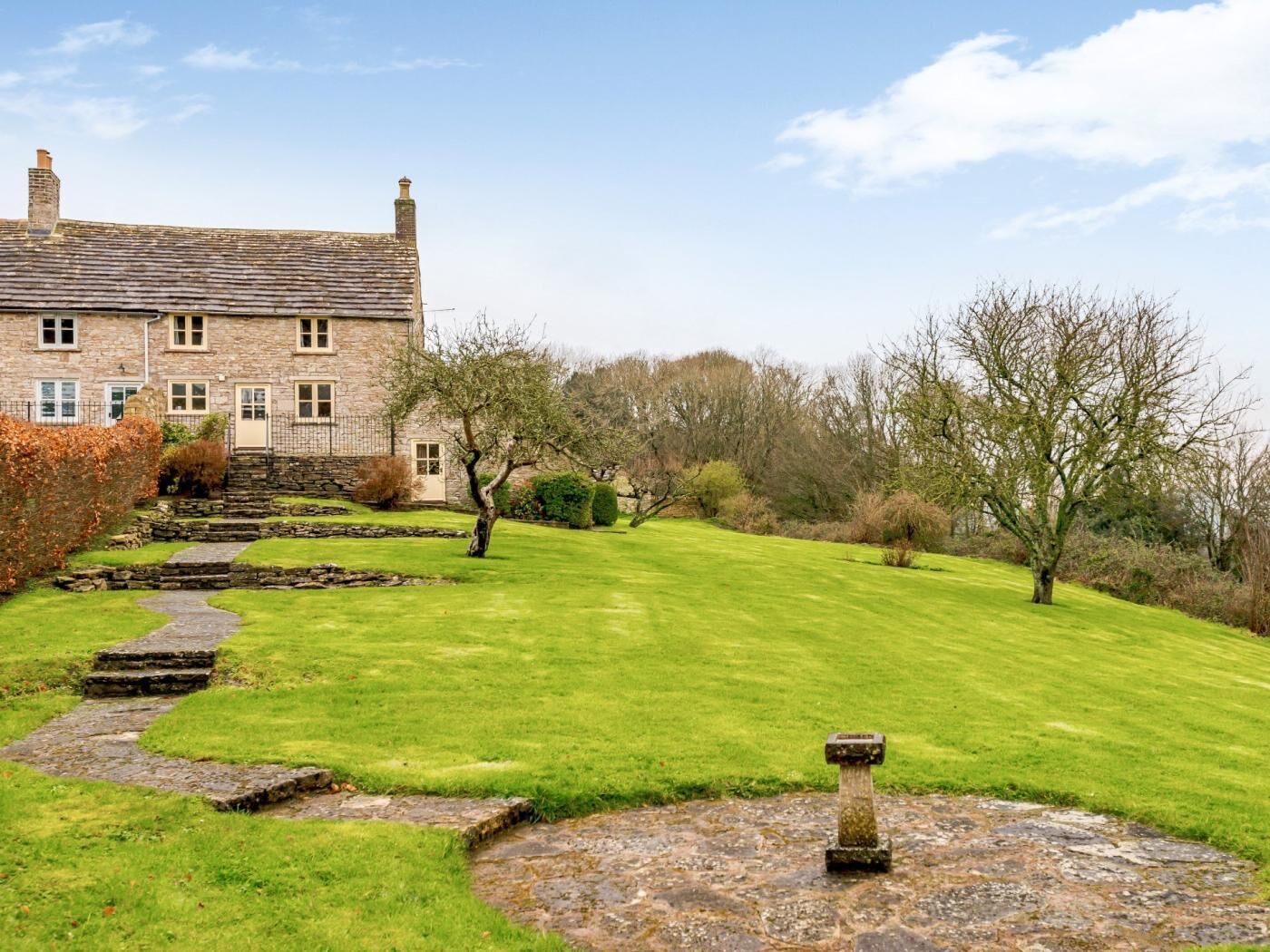 A stone building with a stone staircase leading to a door, surrounded by a well-maintained lawn and trees.