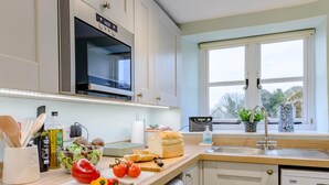 A modern kitchen with a microwave, oven, and dishwasher. There is a window with a view of greenery outside. - 4 Bed in Wareham (oc-78042) (Kingston)