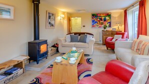 A cozy living room with a fireplace, a sofa, a red chair, and a coffee table with cups and saucers. - 4 Bed in Wareham (oc-78042) (Kingston)