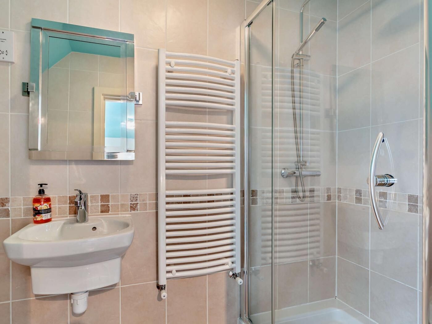 Une salle de bain avec une douche à parois de verre, un lavabo blanc et un porte-serviettes.