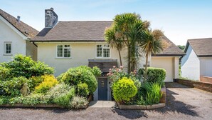 A two-story house with a front door, a garage, and a well-maintained garden with various plants and a palm tree. - 3 Bed in Branscombe (oc-78002) (Branscombe)