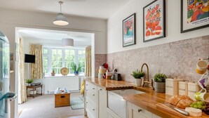 A kitchen with a wooden countertop, a sink, and cabinets. There are potted plants, a radio, and kitchen utensils on the counter. - 3 Bed in Branscombe (oc-78002) (Branscombe)