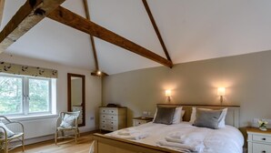 Ein Schlafzimmer mit einem hölzernen Bett, einem Fenster, einem Sessel, einer Kommode und zwei Nachttischlampen.