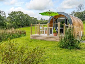 A modern, semi-circular wooden structure with a deck, a table, and a chair.