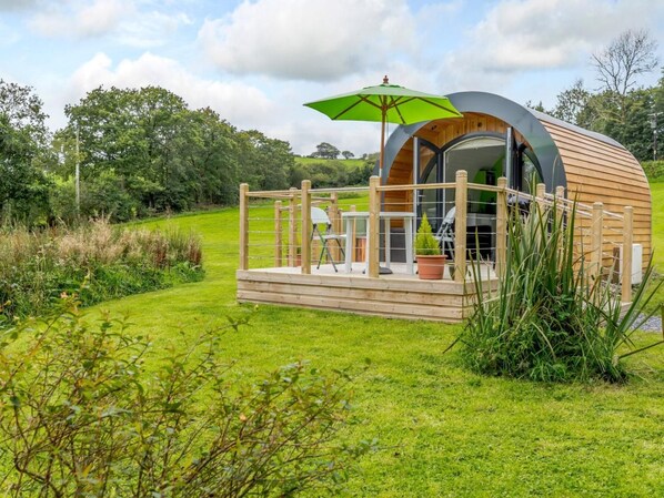 A modern, semi-circular wooden structure with a deck, a table, and a chair.